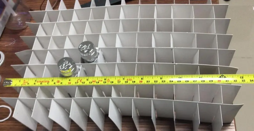 White cell partitions holding glass jars, with a tape measure